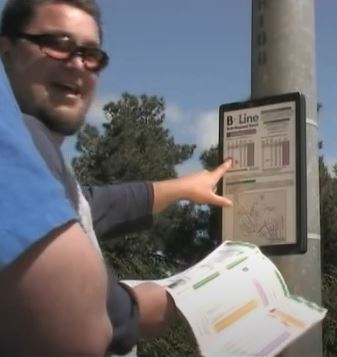 man with bus schedule pointing at pole with bus schedule sign